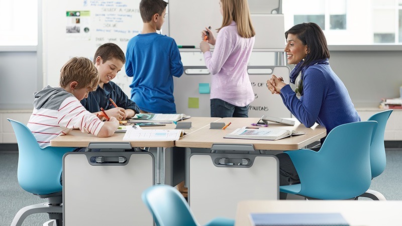 teach sitting with students at modern classroom desk to show classroom furniture ideas