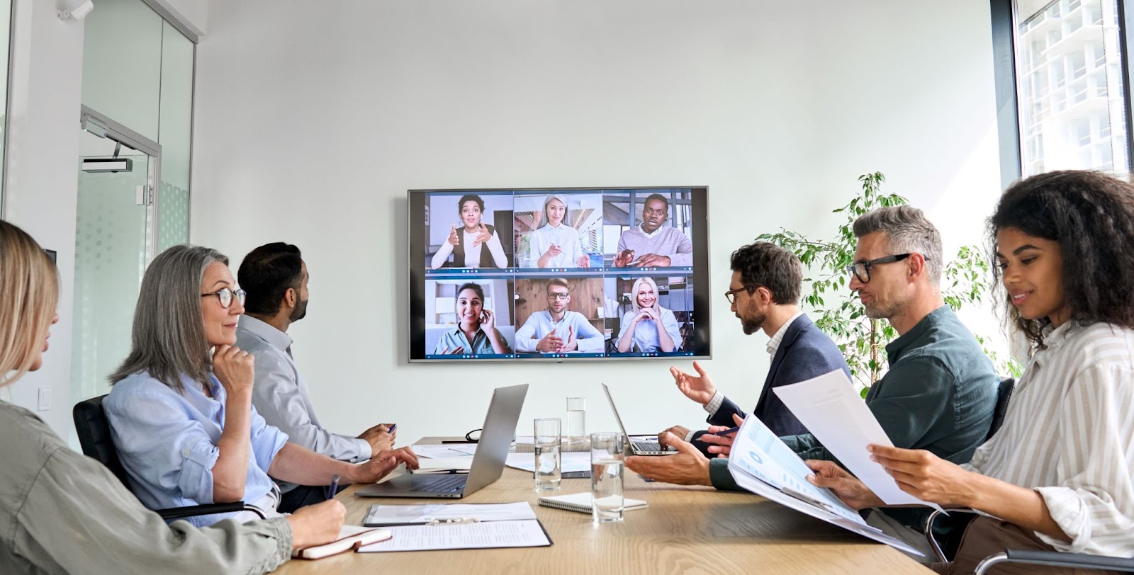 clients in a law office sitting around a conference table while having a virtual conference on a television on the wall