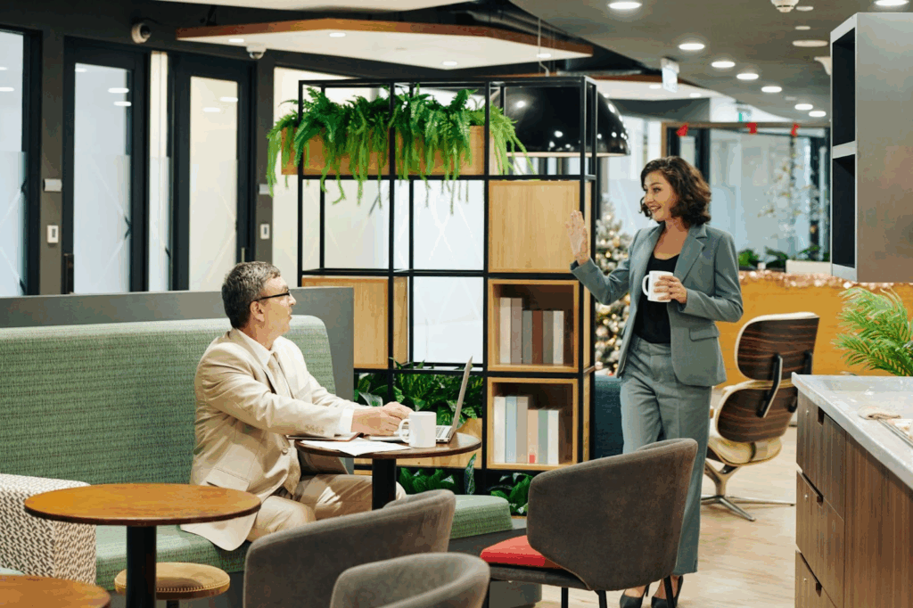 relaxing room with comfortable breakroom furniture, plants on shelf, two coworkers drinking coffee
