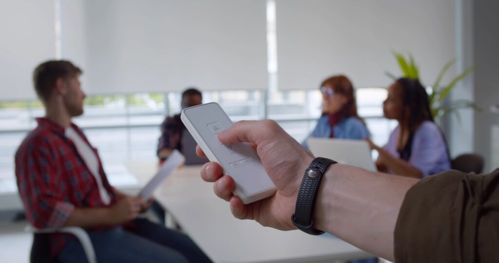 man using remote control to put motorized shades down during an office meeting